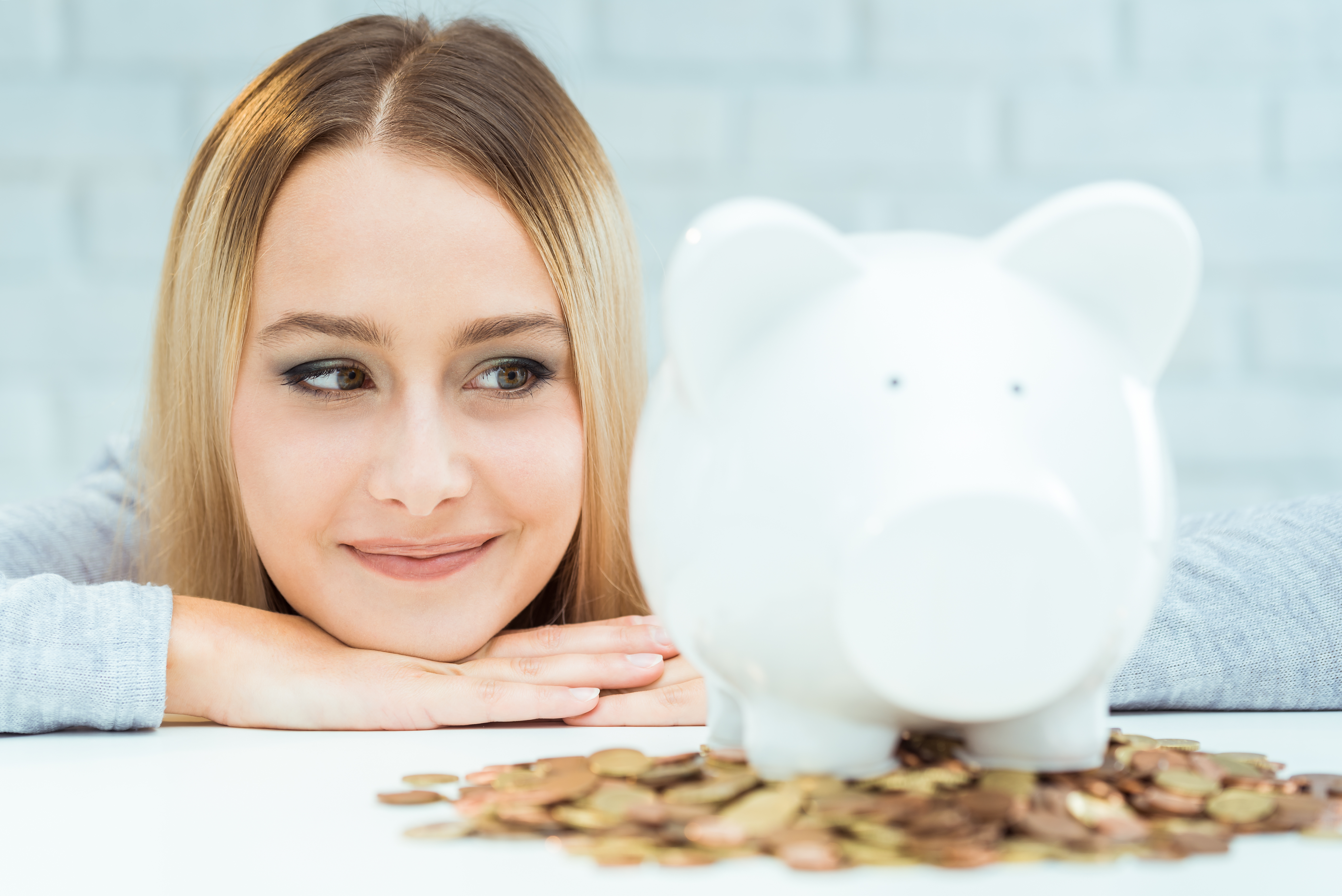 Young blond woman in front of a piggy bank